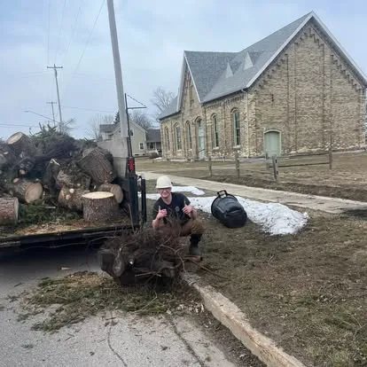 Crew member beside a freshly cleared pile of logs and brush, Manistee, MI